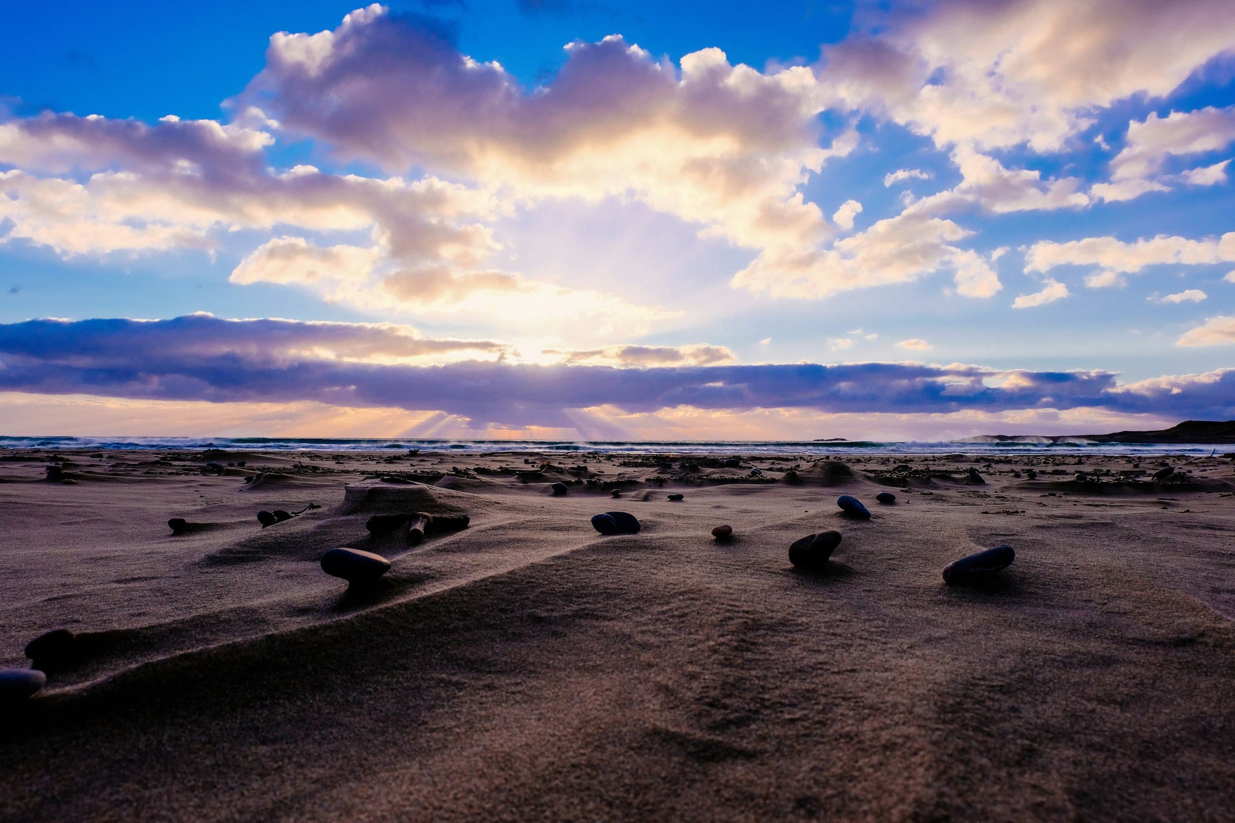 Sunlight breaking through clouds over a sandy beach.